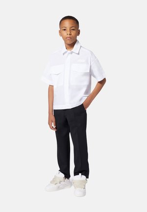 Camicetta bianca a maniche corte con due taschini sul petto, abbinata a pantaloni neri. Calzature sono sneakers bianche con dettagli grigi testurizzati.