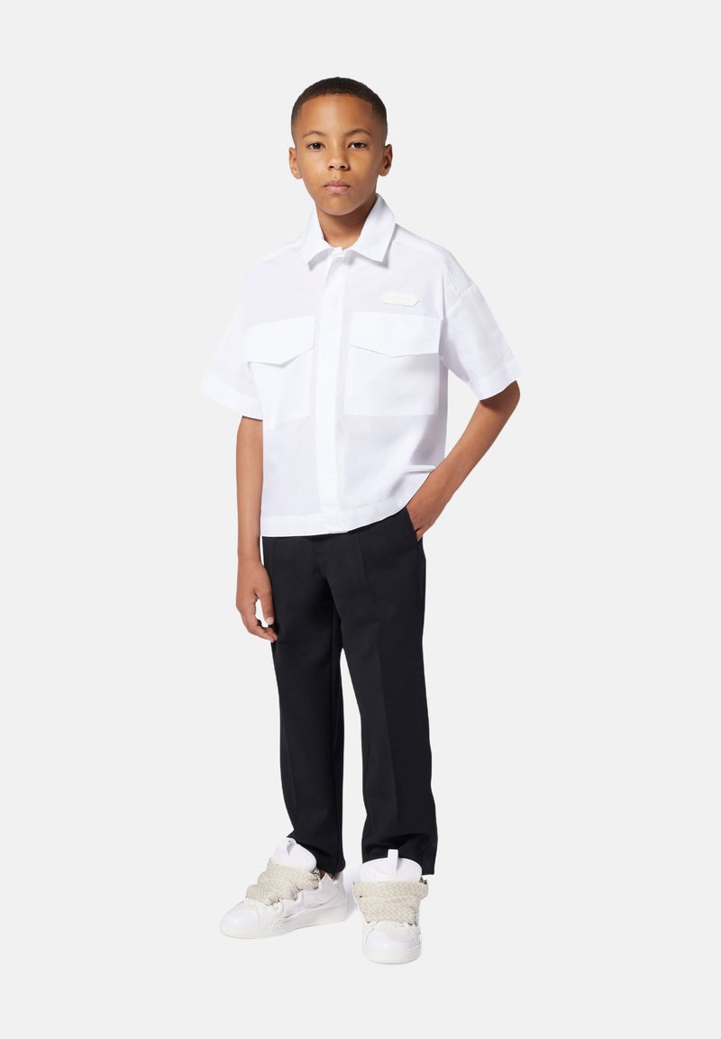 Witte short-sleeve shirt met twee borstzakken, gecombineerd met zwarte broeken. Schoeisel zijn witte sneakers met gestructureerde grijze accenten.