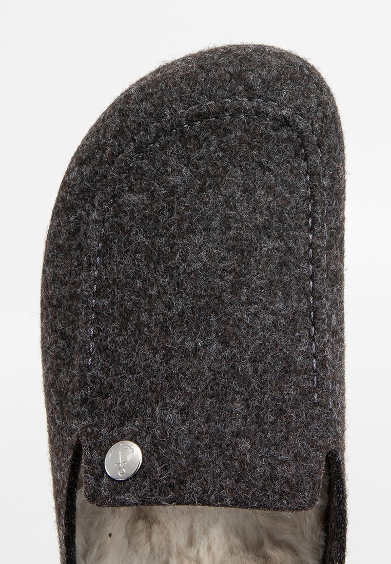 Donkergrijze vilten pantoffel met een gladde textuur, ronde neus en contrasterende stiksels. Bevat een zilveren ronde accent aan de zijkant.
