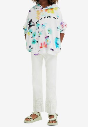 Sweat à capuche blanc avec imprimés floraux colorés et texte noir, assorti à un pantalon blanc orné d'une broderie de palmier et des sandales vert clair.