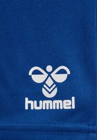 Tela azul con un patrón texturizado y un diseño de logotipo blanco que presenta alas estilizadas y la palabra "hummel" debajo.