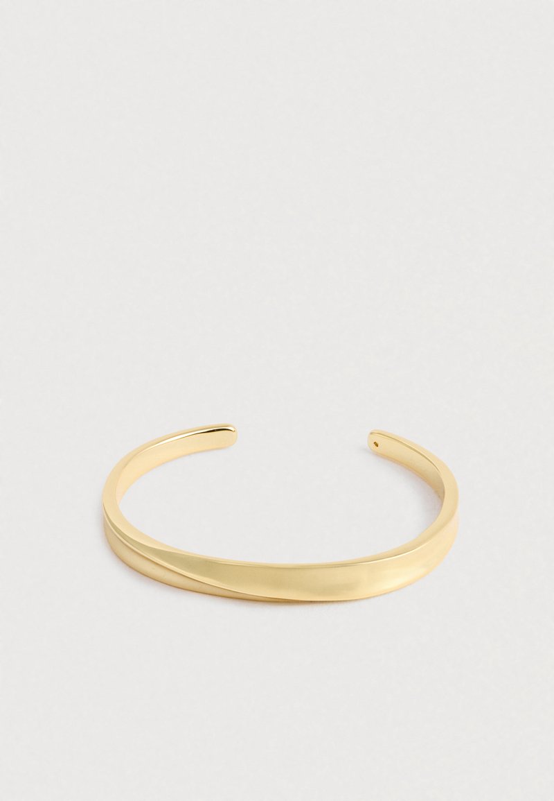 Λείο, γυαλισμένο χρυσό περιβραχιόνιο με ελαφρώς στριμμένο σχέδιο, ανοιχτό στο τέλος για ρυθμιζόμενη εφαρμογή, σε απλό ανοιχτό φόντο.