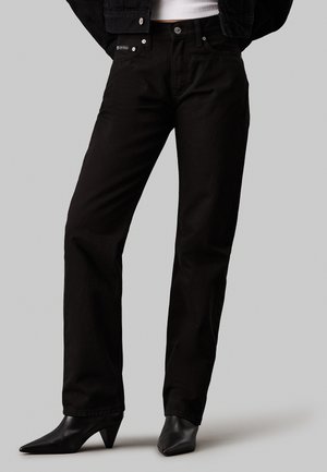 Vaqueros de mezclilla negra con corte recto, diseño de cinco bolsillos y herrajes de marca, combinados con tacones negros puntiagudos.