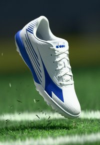 White athletic shoe with blue accents and perforated design, featuring laces and a textured sole for traction on grass surfaces.