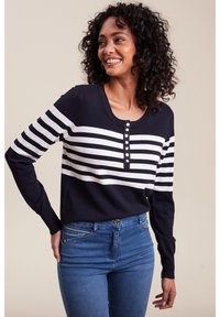 Navy- und weiße gestreifte Strickjacke mit rundem Ausschnitt, versehen mit Knopfdetails und langen Ärmeln, getragen mit blauen Jeans.
