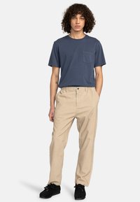 Navy crewneck t-shirt with a chest pocket, paired with light beige tapered trousers and black moccasin shoes, against a white background.
