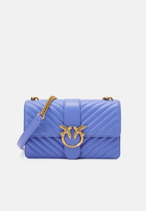 Sac à bandoulière en cuir matelassé lavande avec une chaîne en or et un fermoir en forme d'oiseau doré sur le rabat avant.
