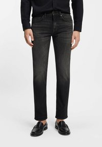 Czarne dżinsy z denimu o prostym kroju, delikatnie sprane, z pięcioma kieszeniami i szlufkami na pasek, noszone z czarnymi skórzanymi mokasynami.