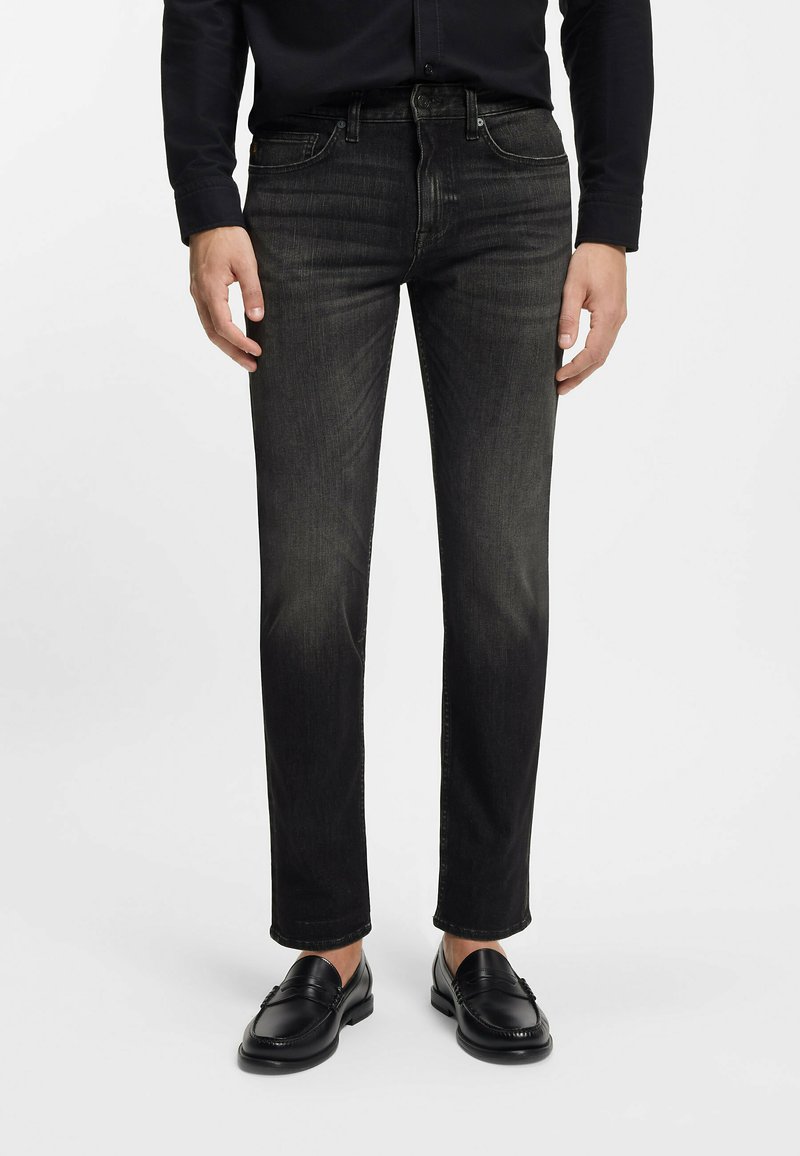 Czarne dżinsy z denimu o prostym kroju, delikatnie sprane, z pięcioma kieszeniami i szlufkami na pasek, noszone z czarnymi skórzanymi mokasynami.