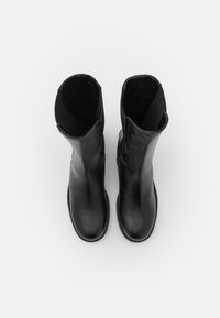 Botas negras de cuero hasta el tobillo con un acabado liso, punteras redondeadas y paneles laterales elásticos. El diseño presenta un tacón bajo y costuras reforzadas.