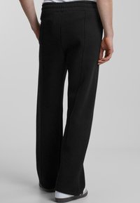 Black sweatpants with a relaxed fit, featuring a drawstring waistband and subtle stitching details. Smooth fabric texture, wide leg design.