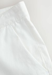 Valged linased püksid, millel on sile tekstuur, lame eesmine vöökoht ja küljetaskud, mis näitavad puhtaid ja lihtsaid disainijooni.