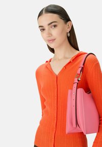 Hoody oranje geribde cardigan met knoopsluiting, gecombineerd met een gestructureerde roze leren handtas met een contrasterende rand en verstelbare schouderriem.