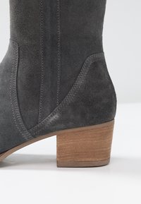 Szare zamszowe botki za kostkę z solidnym drewnianym obcasem. Posiadają kontrastowe przeszycia i gładkie wykończenie po bokach. Miękka tekstura na całej powierzchni.