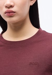 Κοντινό πλάνο ενός ατόμου που φοράει μπορντό μπλουζάκι με τη λέξη «BOSS» κεντημένη στο στήθος.