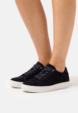 Marineblå ruskinds sneakers med en flad hvid gummisåle, rund tå og grå snørebånd. Minimalistisk design, lav skæring ved anklen.