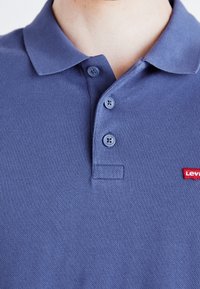 Polo bleu foncé en tissu texturé, avec une patte de boutonnage à trois boutons et un petit logo Levi's rouge sur le côté gauche.