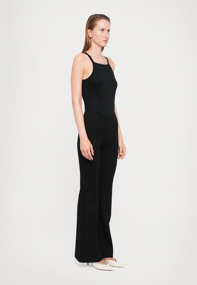 Black fitted tank top with narrow straps, paired with high-waisted black flared pants. Model wearing cream-colored heels.
