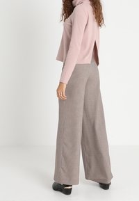 Jasnoróżowy sweter z golfem w prążki z rozcięciem z tyłu, zestawiony z szerokimi spodniami w wzór houndstooth w neutralnych odcieniach. Czarne obuwie.