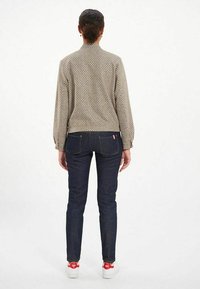 Blouse à manches longues à motifs avec un col, associée à un jean slim bleu foncé et des baskets blanches avec des accents rouges.