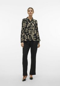 Sort bluse med cremede blomsterprint, lange ærmer, knaplukning foran, parret med sorte lige ben bukser og sorte hæle mule-sko.