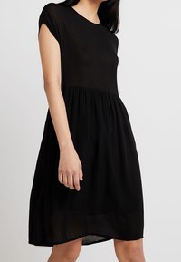 Schwarzes, kurzärmliges Kleid mit rundem Ausschnitt und locker fließendem Rock. Hergestellt aus einem leichten Stoff, zeichnet sich durch ein einfaches, klassisches Design aus.