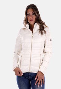 Giacca imbottita di colore crema con cappuccio, chiusura con zip e dettagli in metallo dorato. Presenta una texture trapuntata e due tasche laterali con zip.
