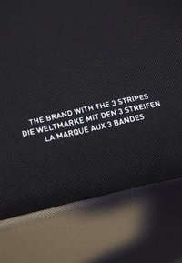 Vit text på engelska, tyska och franska på svart tyg läser "Varumärket med de 3 ränderna" på tre språk.