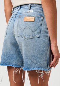 Shorts in denim azzurro chiaro con orlo sfrangiato, dotati di una patch in pelle marrone Wrangler e cuciture a contrasto sulle tasche posteriori.