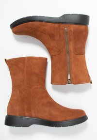 Bruine suède enkelboots met een zwarte rubberen zool, voorzien van een zijrits en gestikte details op de schacht. Platte en ronde neusdesign.