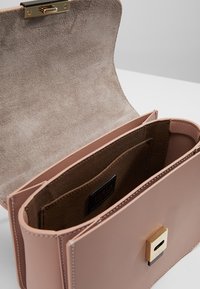 Růžová kožená kabelka se strukturovaným tvarem, hladkým povrchem a vyplněním z nubuku. Má zlaté uzavření na klips a značkovou visačku.