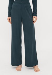 Pantalons larges en teal foncé en tissu c�ôtelé doux, dotés d'une taille ajustée avec un bord volanté et de fentes sur les côtés à l'ourlet.