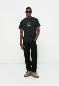 Camiseta negra de manga corta con un diseño gráfico amarillo que presenta el texto "FORMER". Combinada con pantalones negros y botas de tobillo beige.