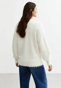 Suéter blanco esponjoso con mangas largas y sueltas y dobladillo acanalado, combinado con jeans de mezclilla azules. La textura suave y el ajuste holgado son características notables.