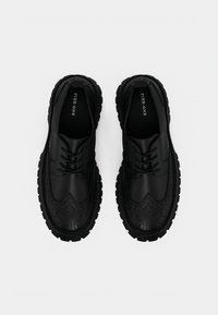 Μαύρα παπούτσια με κορδόνια και σχέδιο μπροκ, κατασκευασμένα από λείο δέρμα, με χοντρή σόλα από καουτσούκ και στρογγυλεμένη μύτη.