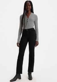 Jeans negros de tiro alto combinados con una camiseta de manga larga henley a rayas gris y blanca. La modelo lleva botas negras hasta el tobillo.