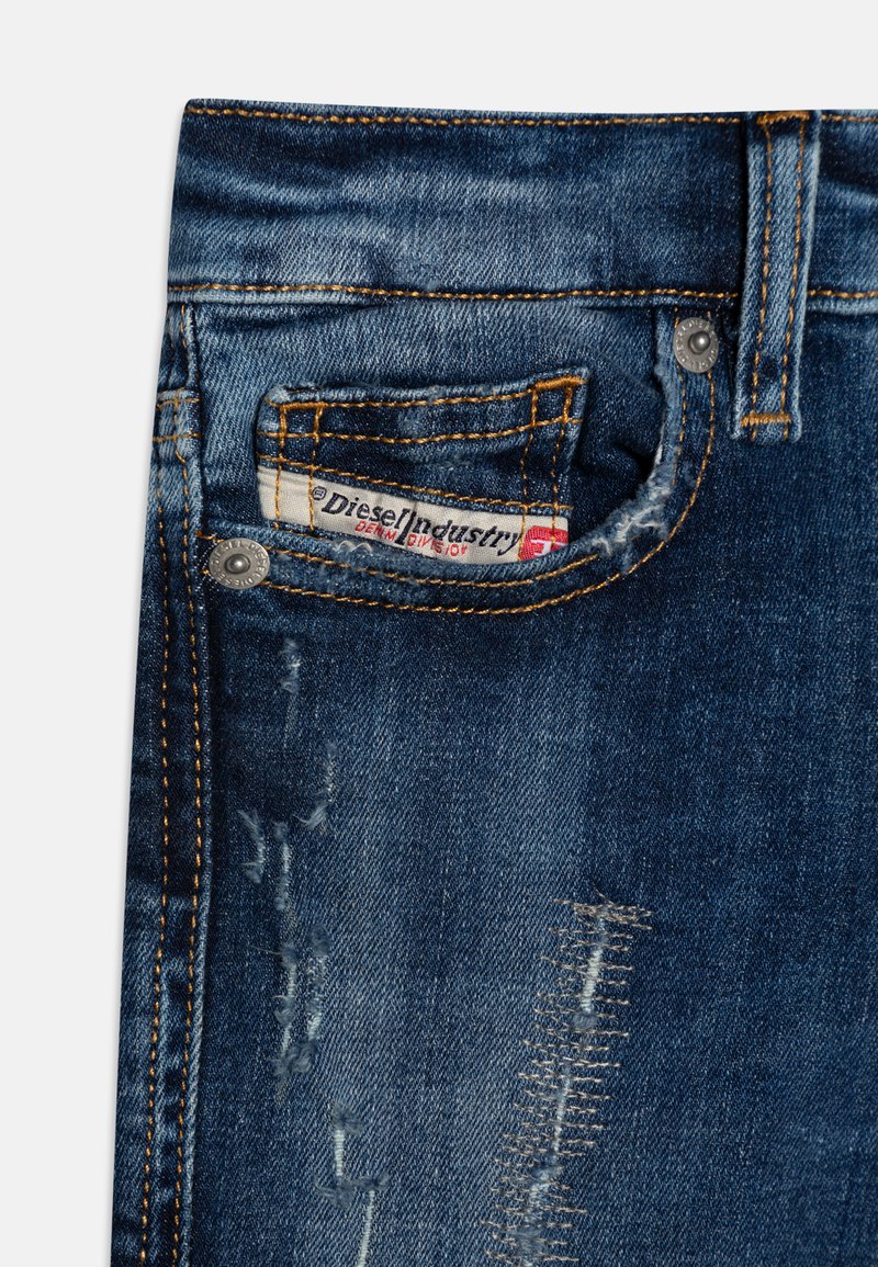 Jeans in denim blu scuro con dettagli strappati, cuciture arancioni e un'etichetta con il marchio nella tasca anteriore. Presentano accessori in metallo.