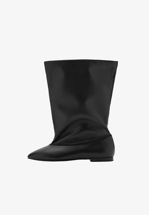 Botín de cuero negro con un diseño suave y caído; punta afilada, tacón cuadrado bajo y textura lisa. Presenta un hardware minimalista y sin patrones.