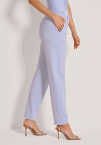 Leicht lavendelfarbene, taillierte Hose mit schmaler Passform, seitlichen Taschen und glatter Textur, kombiniert mit beigen Riemchen-Absätzen.