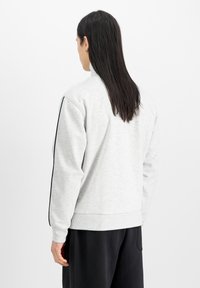 Hellgrauer Sweatshirt mit langen Ärmeln, gerippten Bündchen und hohem Kragen. Verfügt über schwarze Seitenstreifen und einen weichen, strukturierten Stoff.