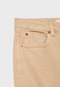 Bež traperice s teksturiranim završetkom, dizajnom s pet džepova,硬ware u boji bakra i vidljivim šavovima.