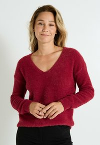 Pull rouge en V en tricot doux et duveteux. Manches longues avec des poignets et un ourlet côtelés. Coupe décontractée, avec une surface texturée pour plus de chaleur.