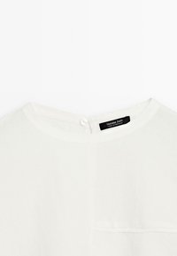 Top blanc avec un col rond et un petit bouton à l'arrière. Une étiquette "Massimo Dutti" est visible près du cou.