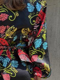 Μαύρο ύφασμα με πολύχρωμο σχέδιο λουλουδιών και χεριών σε κόκκινο, μπλε, κίτρινο και πράσινο, με δέσιμο στη μέση και ρέουσες μανσέτες.