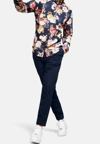 Camicia a fantasia floreale con sfondo blu navy scuro, con fiori rosa, gialli e bianchi. Abbinata a pantaloni blu navy e sneaker bianche.