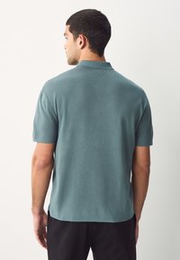 Kurzärmeliges Poloshirt in Petrol mit strukturiertem Strickmuster und klassischem Kragen, von hinten mit lockerer Passform präsentiert.