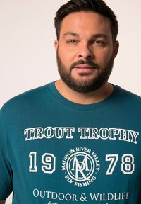 Tyrkysové bavlněné tričko s bílým nápisem "TROUT TROPHY" a čísly "1978" a kruhovým logem. Klasický střih a kulatý výstřih.