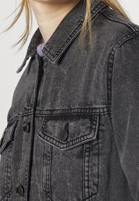 Giacca di jeans nera con finitura testurizzata, dotata di colletto a punta, chiusura con bottoni e due tasche sul petto con alette a punta.