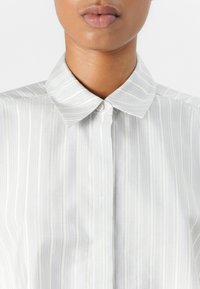 Chemise à rayures bleu clair et blanche, avec un col classique, dotée d'une texture lisse et d'un bouton unique au cou.