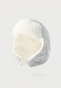 Γκρι καπέλο χειμερινής παγίδας με λευκή επένδυση από φλις και πλαϊνά καλύμματα αυτιών, μπροστινά κουμπιά ασφαλείας, κρεμασμένο σε λευκό φόντο.